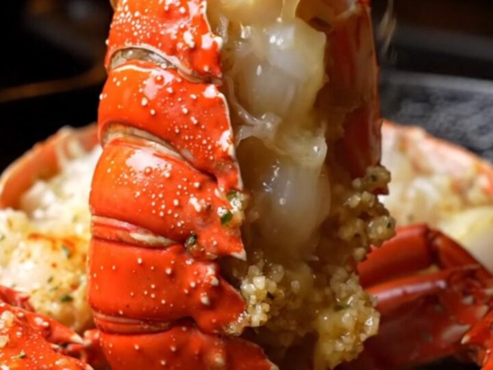 A close-up of a perfectly cooked lobster tail, glistening with garlic butter and fresh herbs.