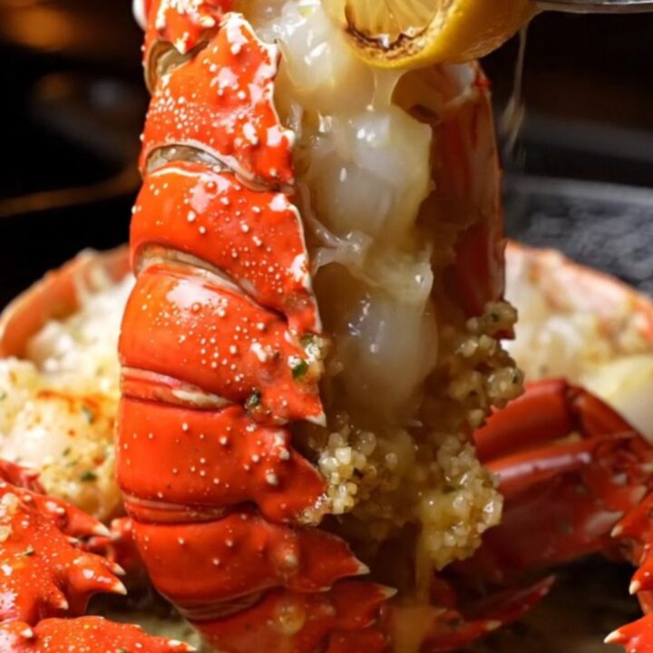 A close-up of a perfectly cooked lobster tail, glistening with garlic butter and fresh herbs.