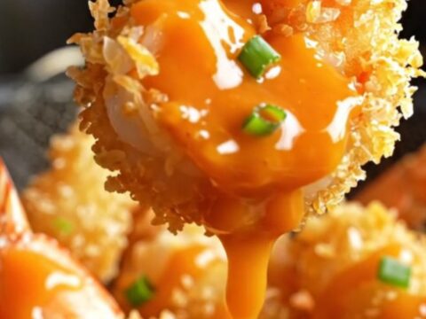 A plate of golden-brown coconut-crusted jumbo shrimp drizzled with spicy-sweet Bang Bang sauce and garnished with sliced