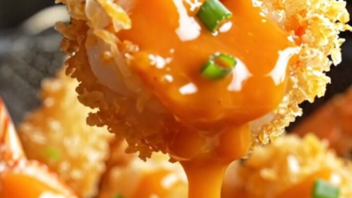 A plate of golden-brown coconut-crusted jumbo shrimp drizzled with spicy-sweet Bang Bang sauce and garnished with sliced
