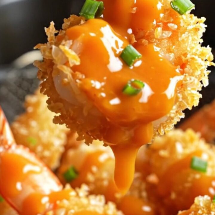 A plate of golden-brown coconut-crusted jumbo shrimp drizzled with spicy-sweet Bang Bang sauce and garnished with sliced