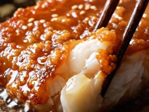 A close-up of a miso-glazed black cod fillet in a cast-iron skillet, showing a caramelized mahogany crust and flaking fish.