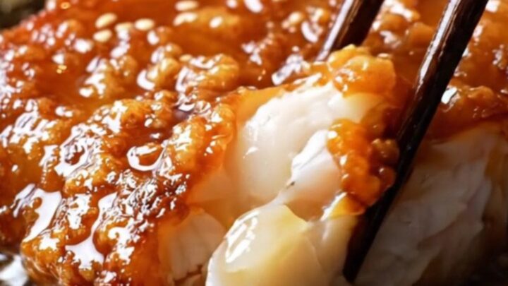 A close-up of a miso-glazed black cod fillet in a cast-iron skillet, showing a caramelized mahogany crust and flaking fish.