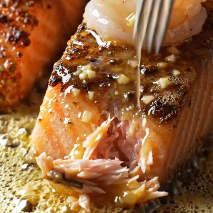 A cast-iron skillet filled with blackened salmon fillets and jumbo shrimp, glazed in a shimmering honey-garlic sauce.