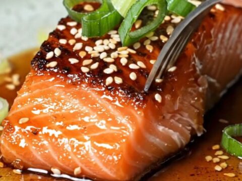 Sticky gochujang maple glazed salmon fillets with crispy blistered skin, garnished with sesame seeds and scallion curls.