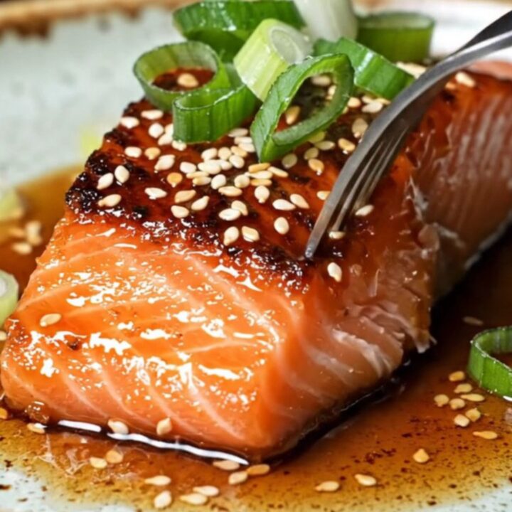 Sticky gochujang maple glazed salmon fillets with crispy blistered skin, garnished with sesame seeds and scallion curls.