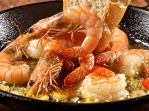 A rustic cazuela filled with sizzling garlic shrimp, vibrant red guindilla chilies, and golden olive oil.