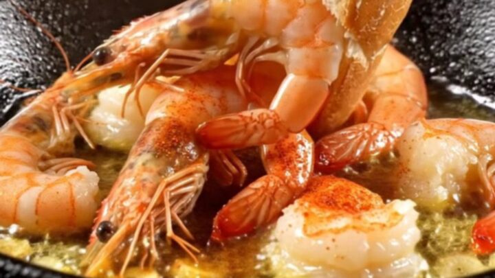 A rustic cazuela filled with sizzling garlic shrimp, vibrant red guindilla chilies, and golden olive oil.