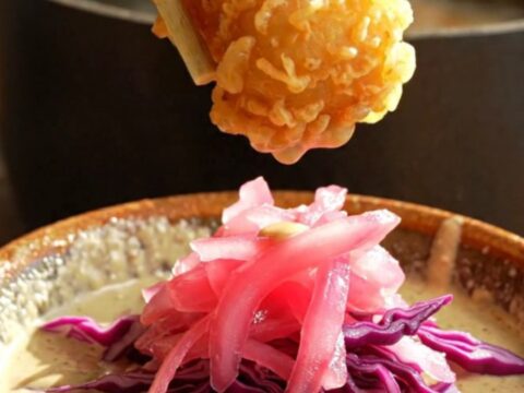 A golden, crispy piece of beer-battered fish being dipped into a creamy, smoky chipotle sauce.