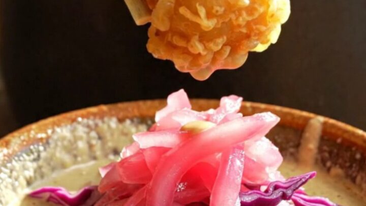 A golden, crispy piece of beer-battered fish being dipped into a creamy, smoky chipotle sauce.