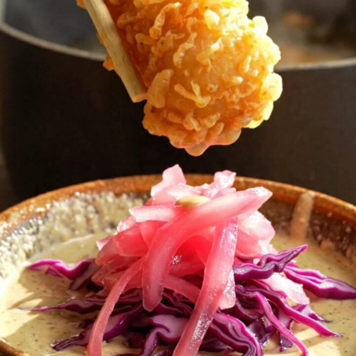 A golden, crispy piece of beer-battered fish being dipped into a creamy, smoky chipotle sauce.