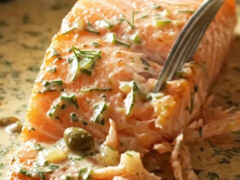 Close-up of a perfectly seared salmon fillet covered in a rich cream sauce with fresh dill and capers.