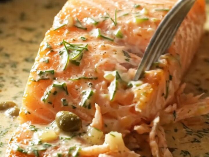 Close-up of a perfectly seared salmon fillet covered in a rich cream sauce with fresh dill and capers.