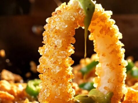 A close-up of golden, crispy salt and pepper calamari rings topped with fried garlic and green jalapeños.
