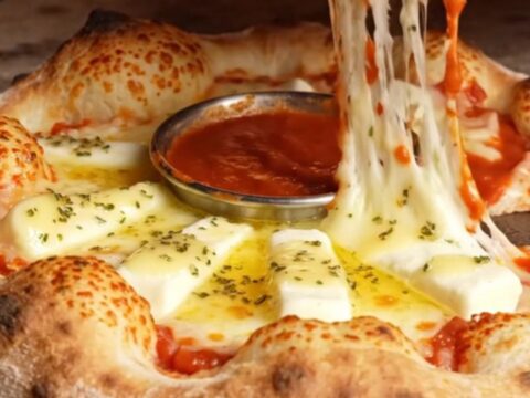 A close-up of a golden brown stuffed crust pizza ring with a molten mozzarella pull.
