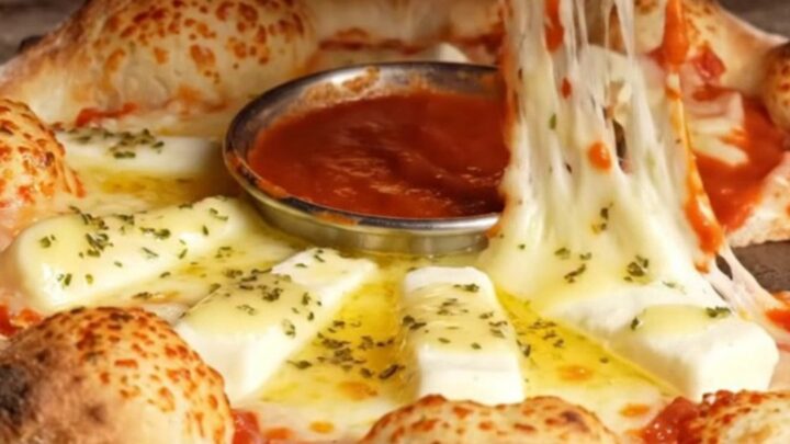 A close-up of a golden brown stuffed crust pizza ring with a molten mozzarella pull.