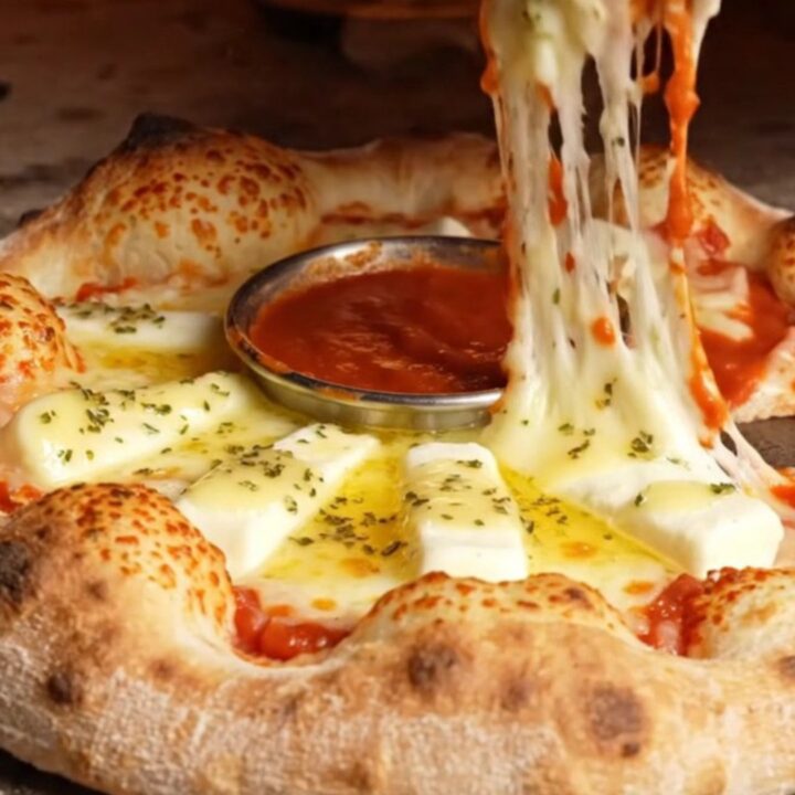 A close-up of a golden brown stuffed crust pizza ring with a molten mozzarella pull.