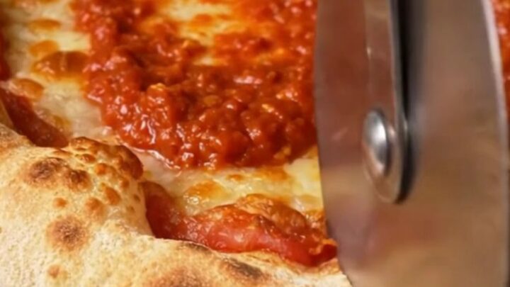 A close-up of a Detroit-style pizza showing the dark amber, lacy caramelized cheese edges and airy crust.