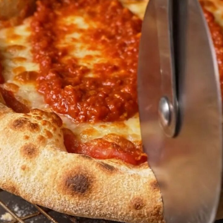A close-up of a Detroit-style pizza showing the dark amber, lacy caramelized cheese edges and airy crust.