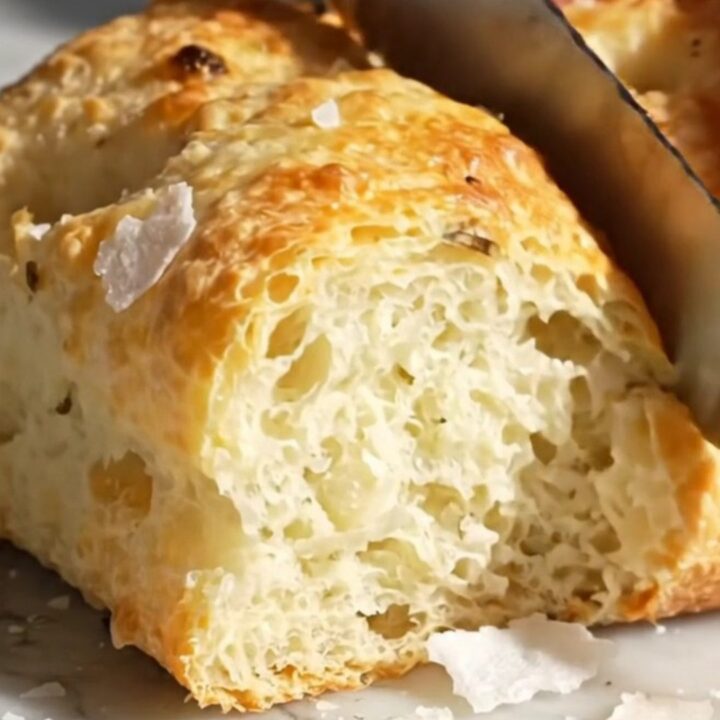 A close-up shot of a freshly baked rosemary focaccia with visible air bubbles and a golden, crispy crust.