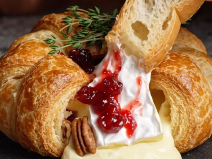 A golden-brown baked brie wheel in puff pastry garnished with fresh thyme on a rustic board.
