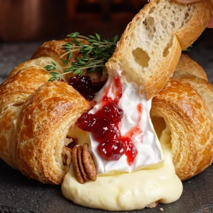 A golden-brown baked brie wheel in puff pastry garnished with fresh thyme on a rustic board.