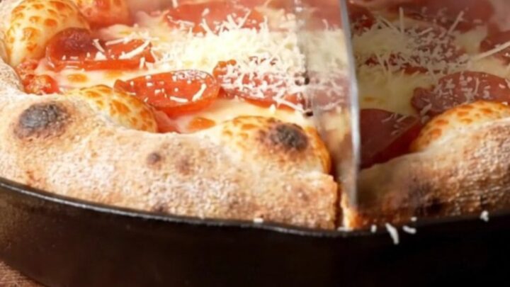 A close-up of an upside-down deep-dish pizza on a wooden board showing a caramelized