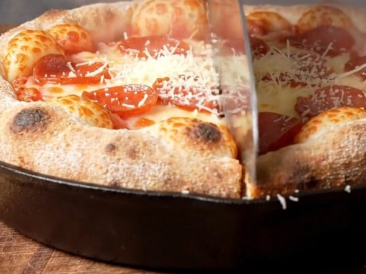 A close-up of an upside-down deep-dish pizza on a wooden board showing a caramelized