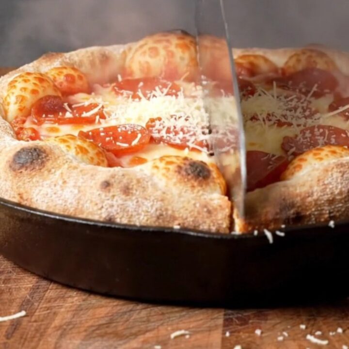 A close-up of an upside-down deep-dish pizza on a wooden board showing a caramelized