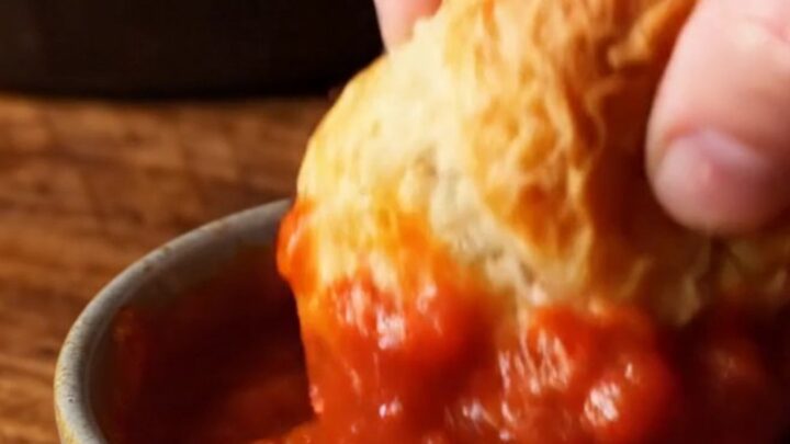 A close-up of a cheesy garlic knot being pulled from the skillet, showing long strings of melted mozzarella.