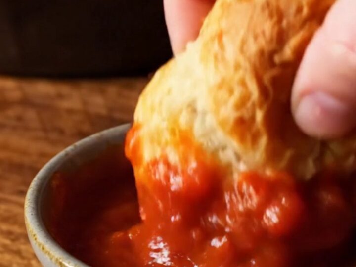 A close-up of a cheesy garlic knot being pulled from the skillet, showing long strings of melted mozzarella.