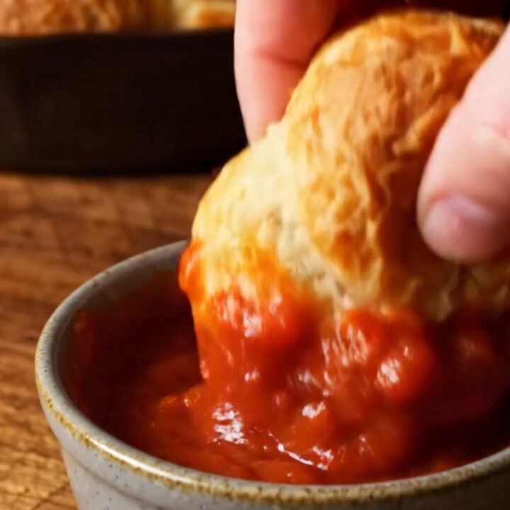 A close-up of a cheesy garlic knot being pulled from the skillet, showing long strings of melted mozzarella.