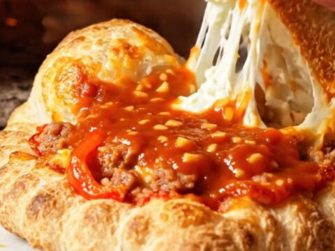 A golden-brown crispy calzone sliced open to reveal a steaming, cheesy ricotta and sausage filling.