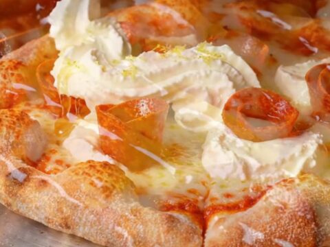 A close-up of a pepperoni pizza slice with charred crispy edges and dollops of white whipped ricotta.