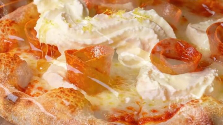 A close-up of a pepperoni pizza slice with charred crispy edges and dollops of white whipped ricotta.
