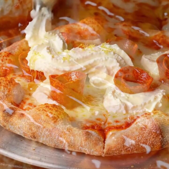 A close-up of a pepperoni pizza slice with charred crispy edges and dollops of white whipped ricotta.