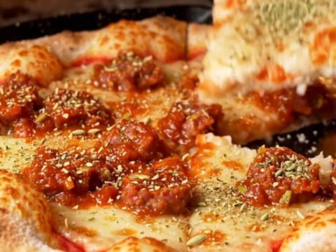 A close-up shot of a square-cut tavern-style pizza showing a thin, crispy crust topped with fennel sausage.