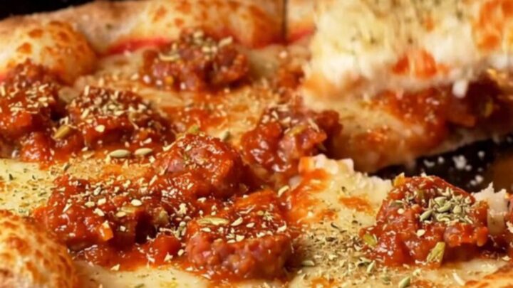 A close-up shot of a square-cut tavern-style pizza showing a thin, crispy crust topped with fennel sausage.
