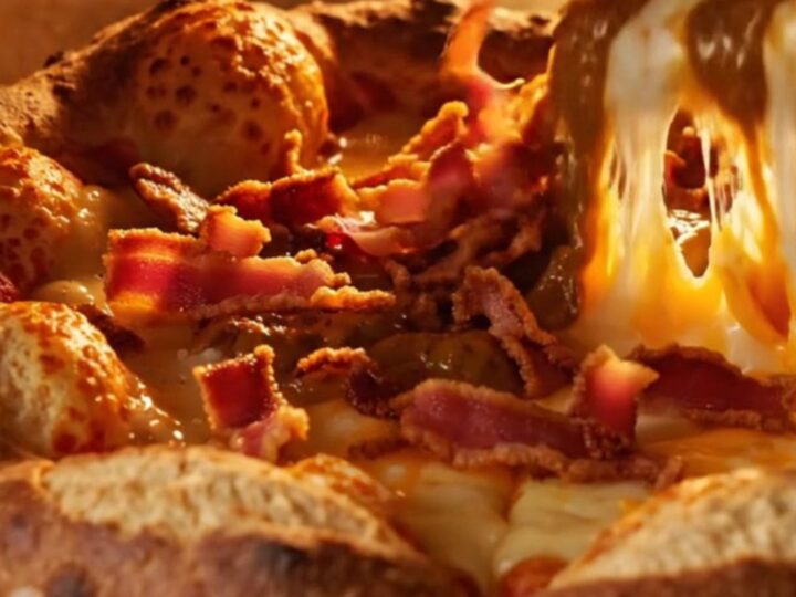 A close-up of a cheddar stuffed pretzel crust pizza slice being pulled away, showing molten cheese.