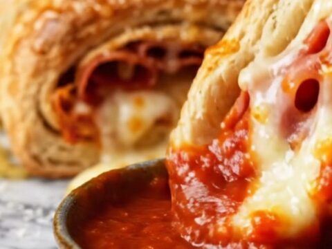 A close-up of a braided Italian stromboli ring, golden brown and sliced to show layers of salami and melted cheese.