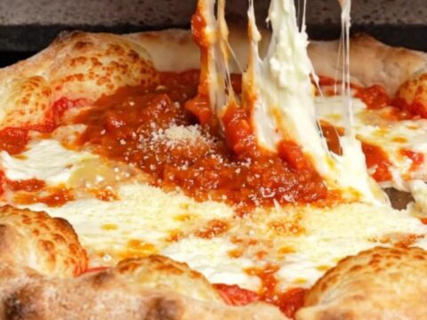 A slice of Chicago-style stuffed pizza lifted from the pan, showing a tall cheese wall and thick tomato sauce.