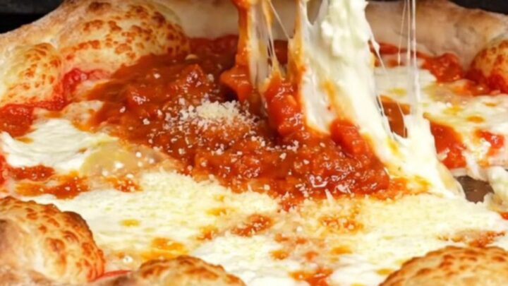 A slice of Chicago-style stuffed pizza lifted from the pan, showing a tall cheese wall and thick tomato sauce.