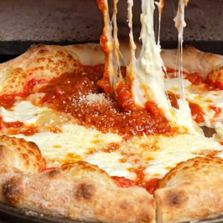 A slice of Chicago-style stuffed pizza lifted from the pan, showing a tall cheese wall and thick tomato sauce.