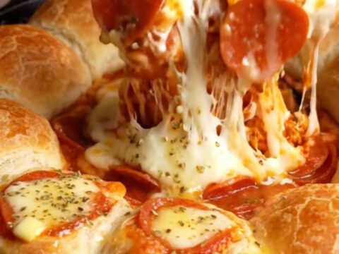 A cast-iron skillet filled with a bubbling cheesy marinara dip surrounded by golden mozzarella-stuffed breadsticks.