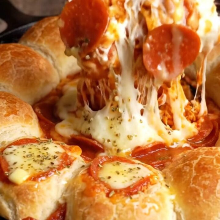 A cast-iron skillet filled with a bubbling cheesy marinara dip surrounded by golden mozzarella-stuffed breadsticks.