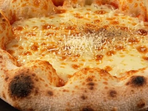 A close-up of a four-cheese stuffed crust pizza with a golden, blistered rim and a drizzle of dark fig glaze.