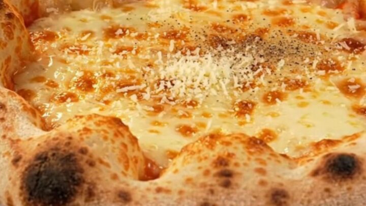 A close-up of a four-cheese stuffed crust pizza with a golden, blistered rim and a drizzle of dark fig glaze.