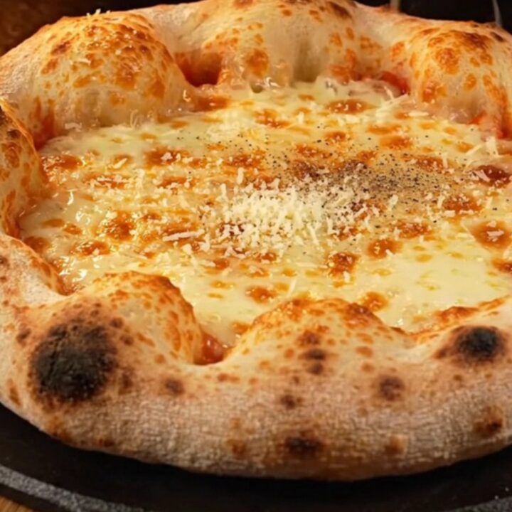 A close-up of a four-cheese stuffed crust pizza with a golden, blistered rim and a drizzle of dark fig glaze.