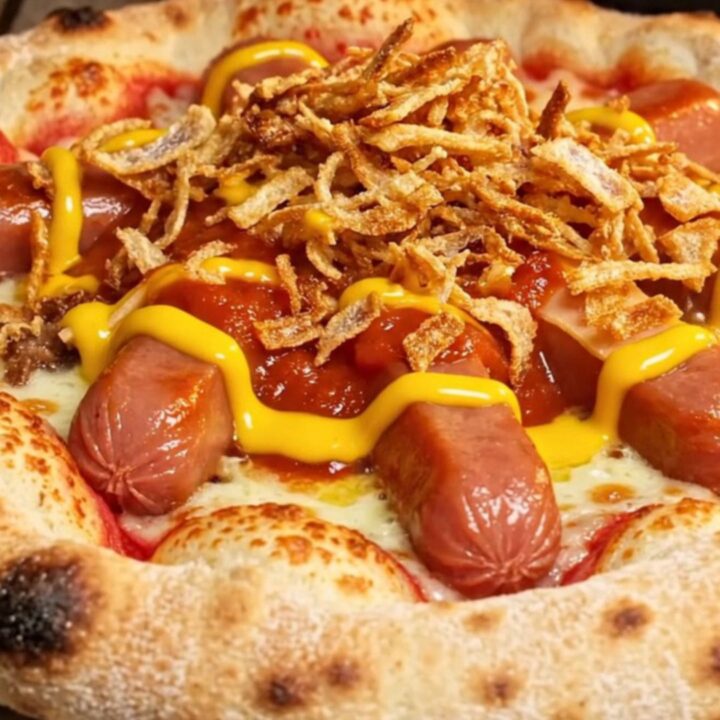 A close-up of a stuffed crust pizza slice being pulled apart, showing melted cheddar and a smoky beef frank inside.