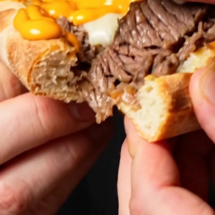 A close-up shot of a Philly cheesesteak stuffed crust pizza showing the melted cheese and ribeye inside the crust.